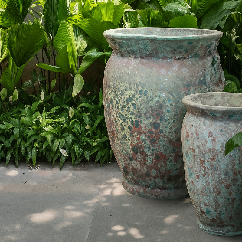 Large rustic garden planters with aged patina finish placed among lush tropical plants in a landscaped outdoor space